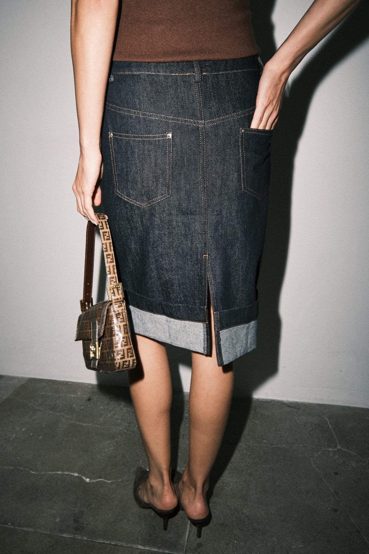 Back view of dark wash denim midi skirt showing the straight silhouette, structured waistband, back pockets, and cuffed hem.