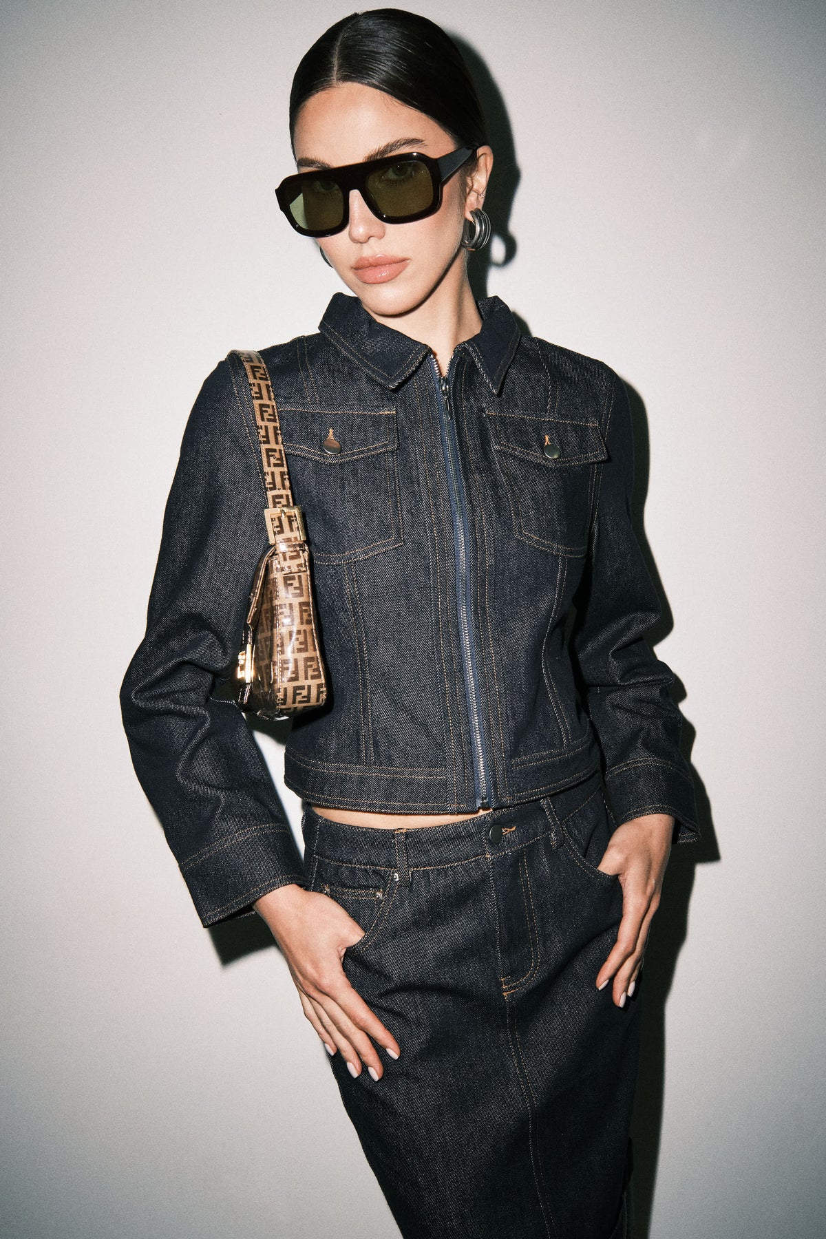 Close-up detail of dark wash denim midi skirt showing the denim texture, contrast stitching, waistband, and pocket detailing.