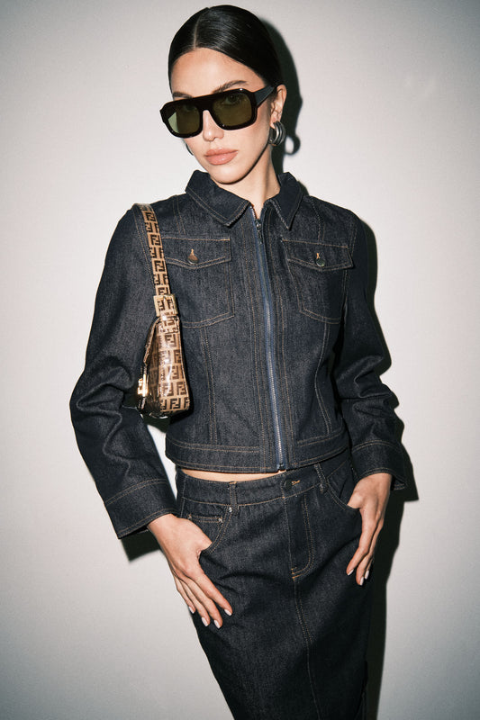 Close-up detail of dark wash denim midi skirt showing the denim texture, contrast stitching, waistband, and pocket detailing.