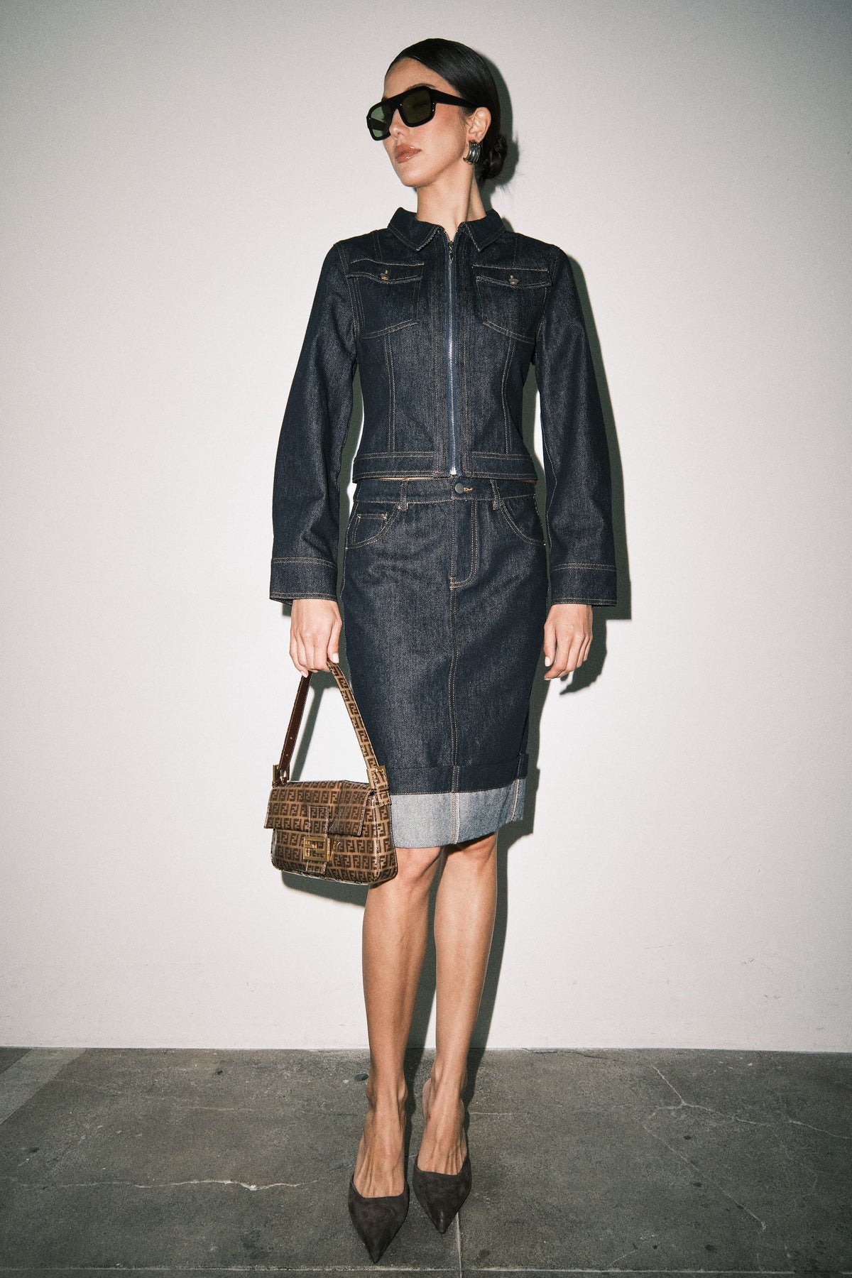 Model wearing a dark wash denim midi skirt with a straight silhouette, classic pockets, structured waistband, and cuffed hem.