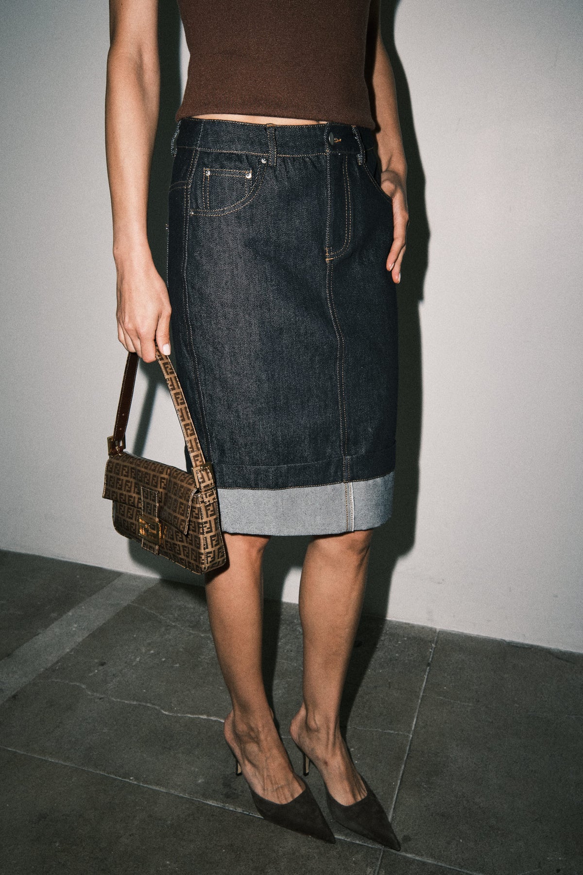 Side view of dark wash denim midi skirt showing its streamlined straight fit, midi length, and structured silhouette.