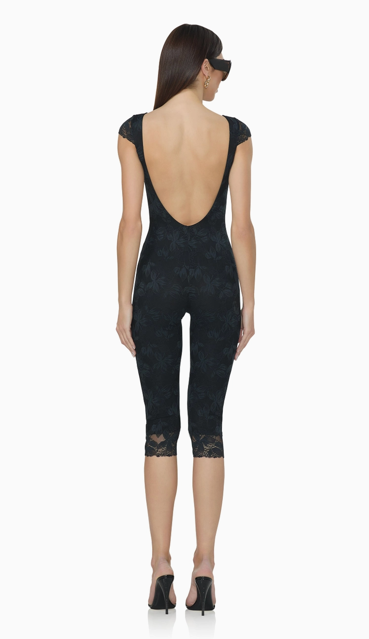 Back view of women's black floral lace catsuit highlighting the dramatic low scoop back, fitted silhouette, and scalloped lace capri hems.