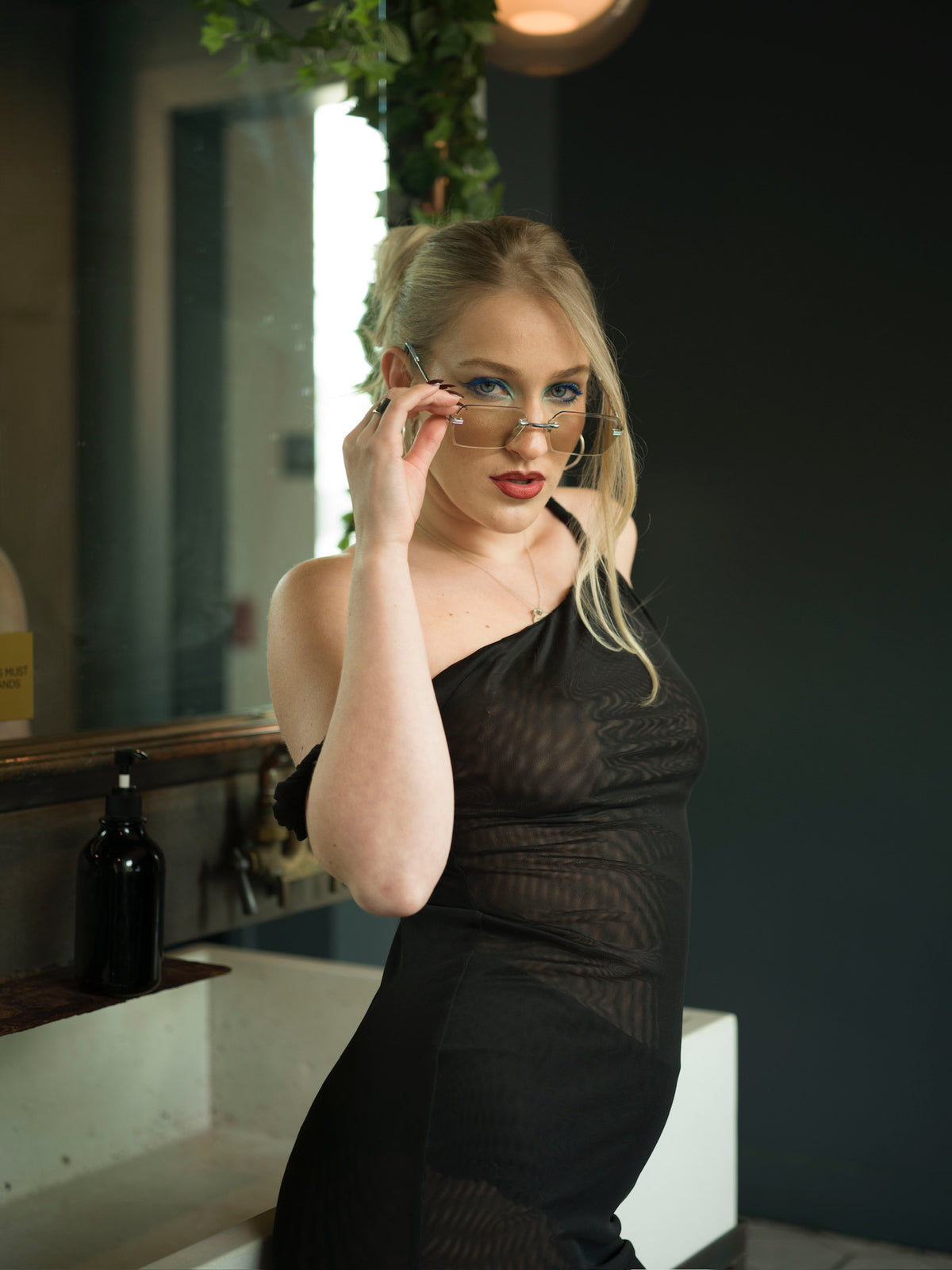 Close-up of black mesh midi dress showing the asymmetrical one-shoulder neckline, off-shoulder strap, and sheer draped fabric.