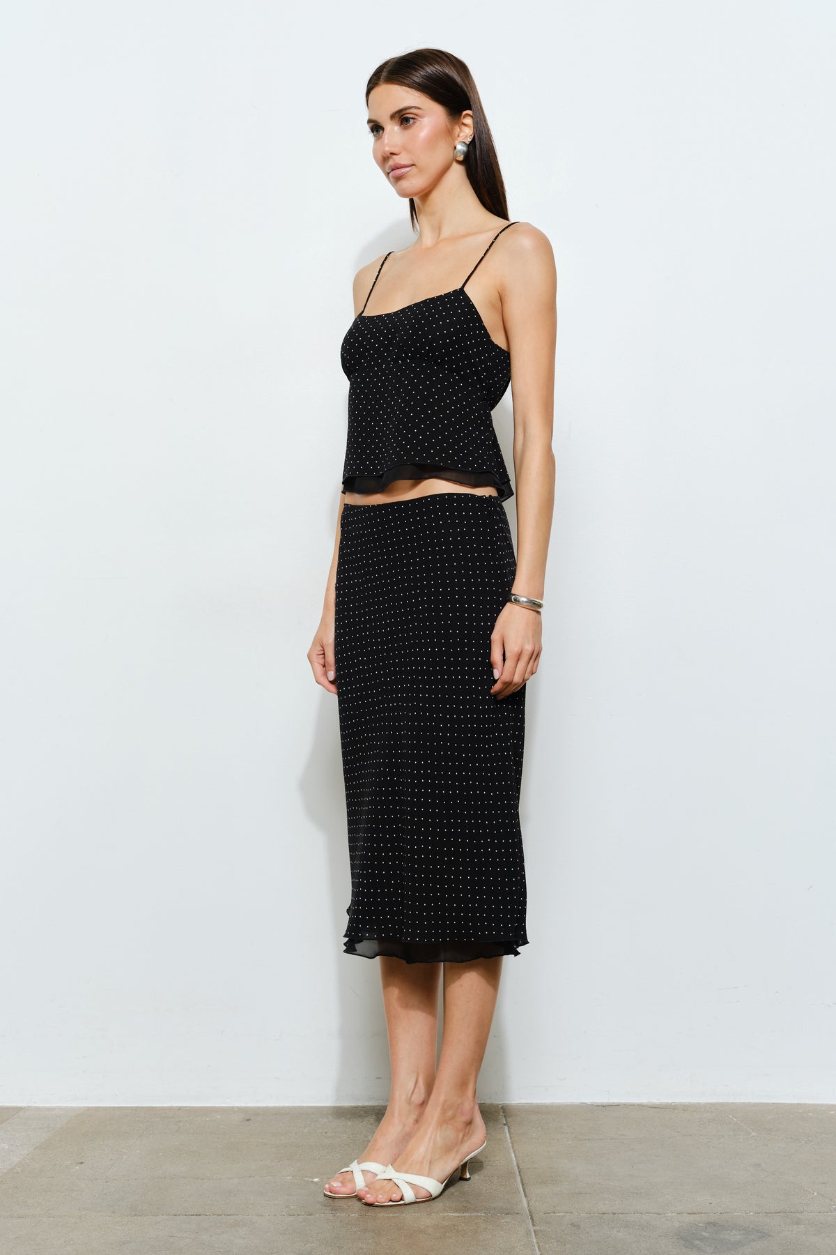Side view of black and white polka dot mesh midi skirt showcasing the fitted shape through the hips and lightly flared hemline.