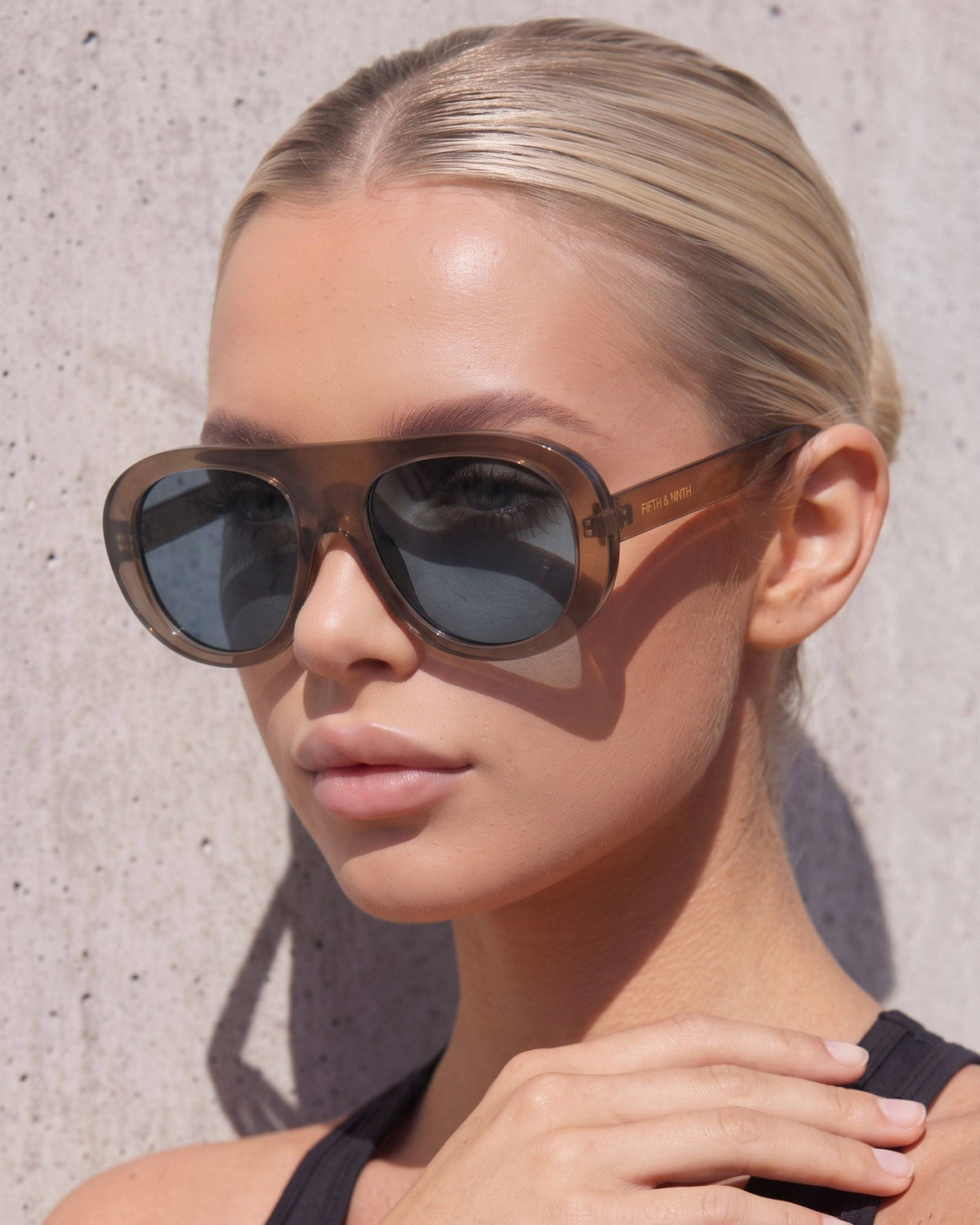 Blonde model wearing Oceane brown polarized aviator sunglasses with blue-toned lenses in a close-up outdoor fashion shot.
