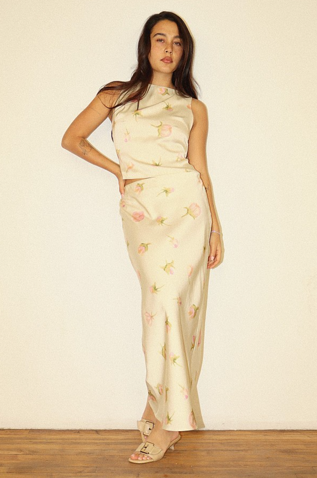 Model wearing a cream and pink floral satin maxi skirt styled with a coordinating floral top and neutral heeled sandals.