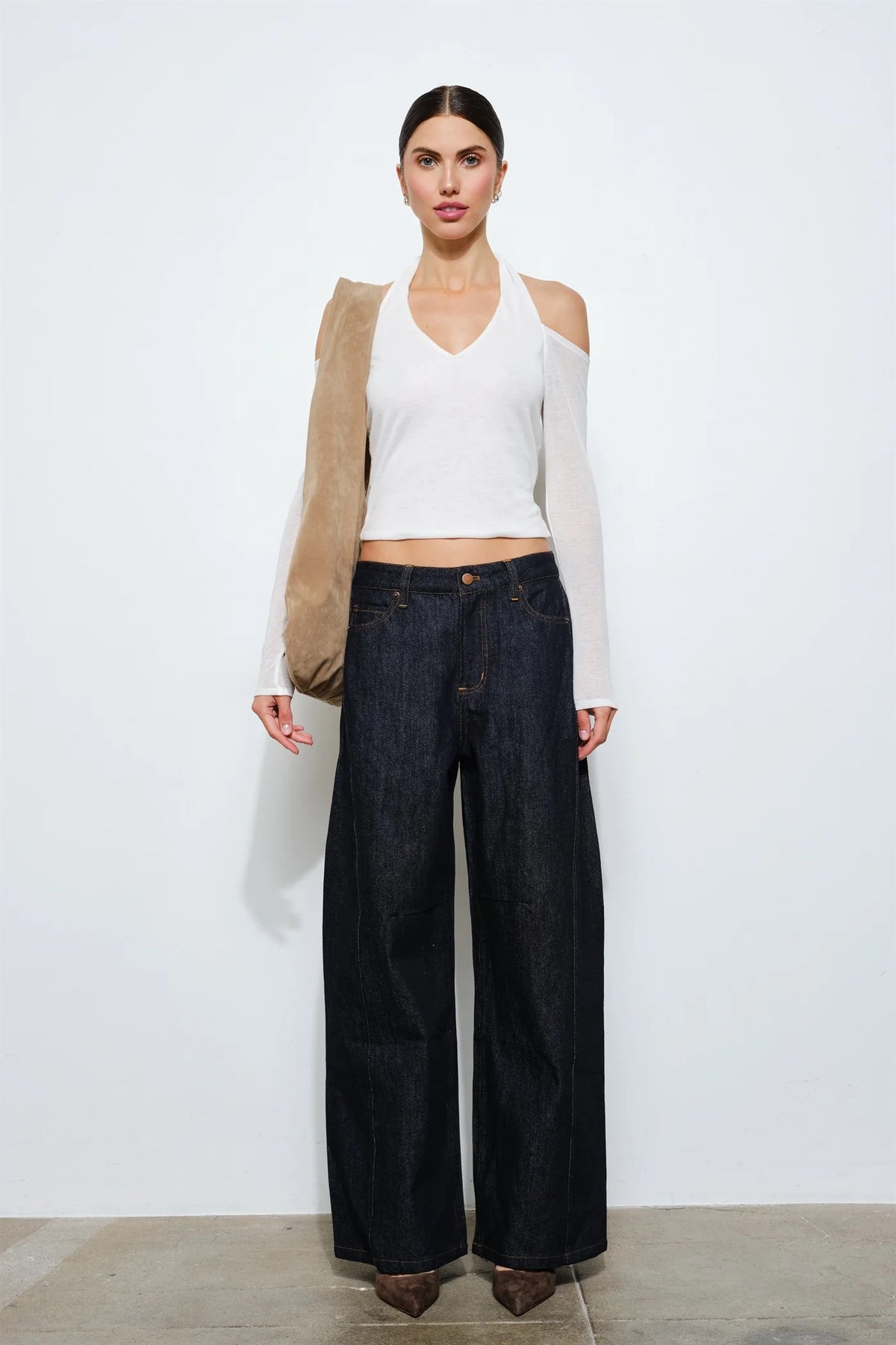 Full body front view of a model wearing a white cropped halter top with long sleeves and open shoulders