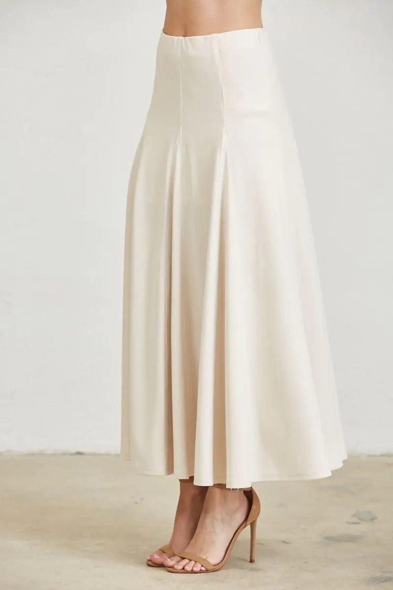 Front view of ivory flared maxi skirt featuring a fitted waist, vertical seam detailing, and an elegant flowing hemline.