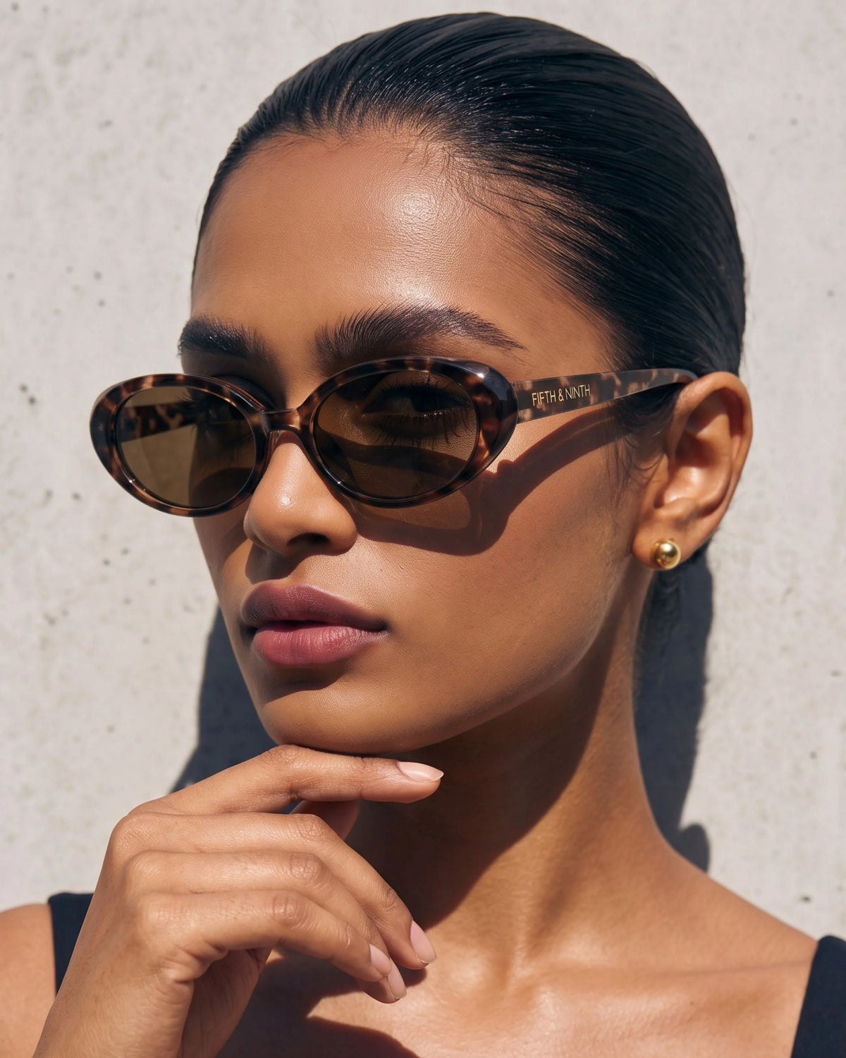 Fashion model styling narrow tortoiseshell oval sunglasses with brown polarized lenses, highlighting the minimalist retro design.