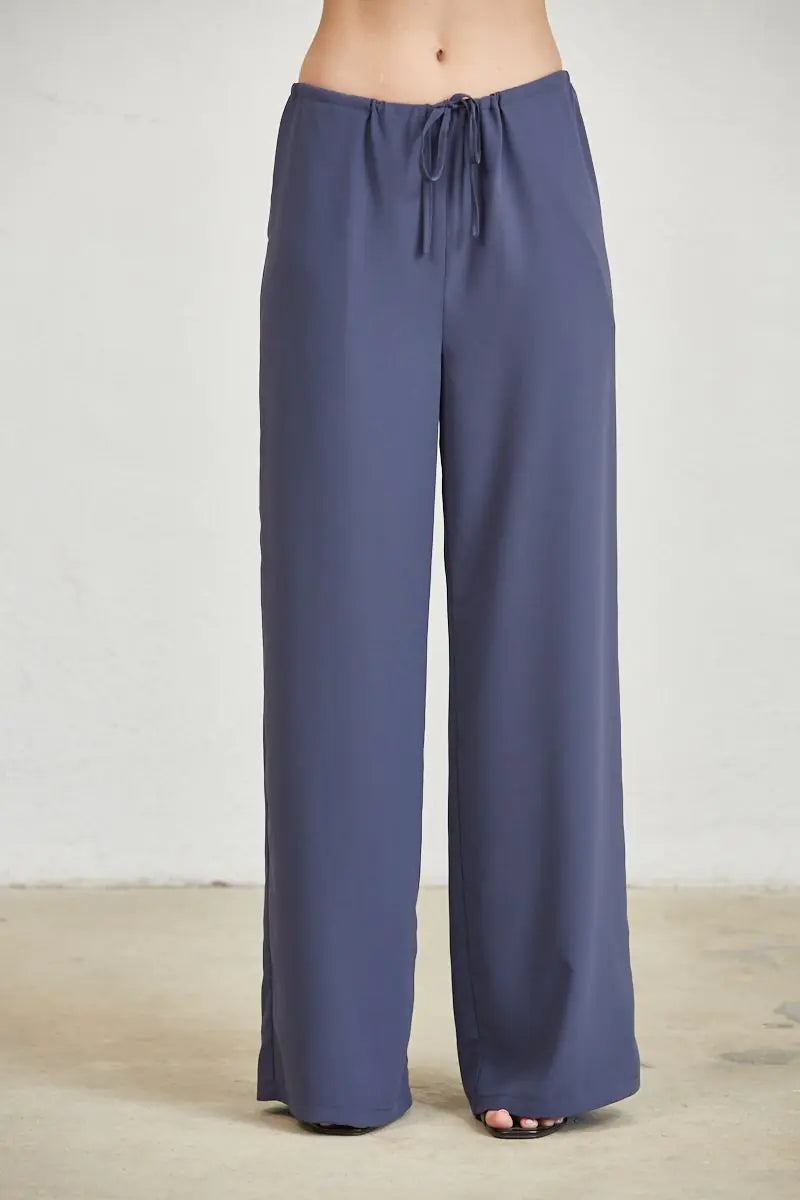 Model wearing slate blue wide leg palazzo pants styled with a coordinating cowl neck halter top and black strappy heels for an elevated monochromatic outfit.